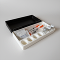 Geöffnete Insulinbox in Weiß mit schwarzem Klappdeckel, Rinnen für Spritzen und Mulden für Ampullen